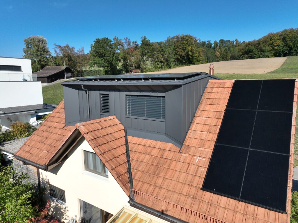 Eine Doppel-Lukarne, verkleidet mit Winkelfalz-Bahnen und Aluverbund-Platten aus dunkelgauem Prefa Aluminium.